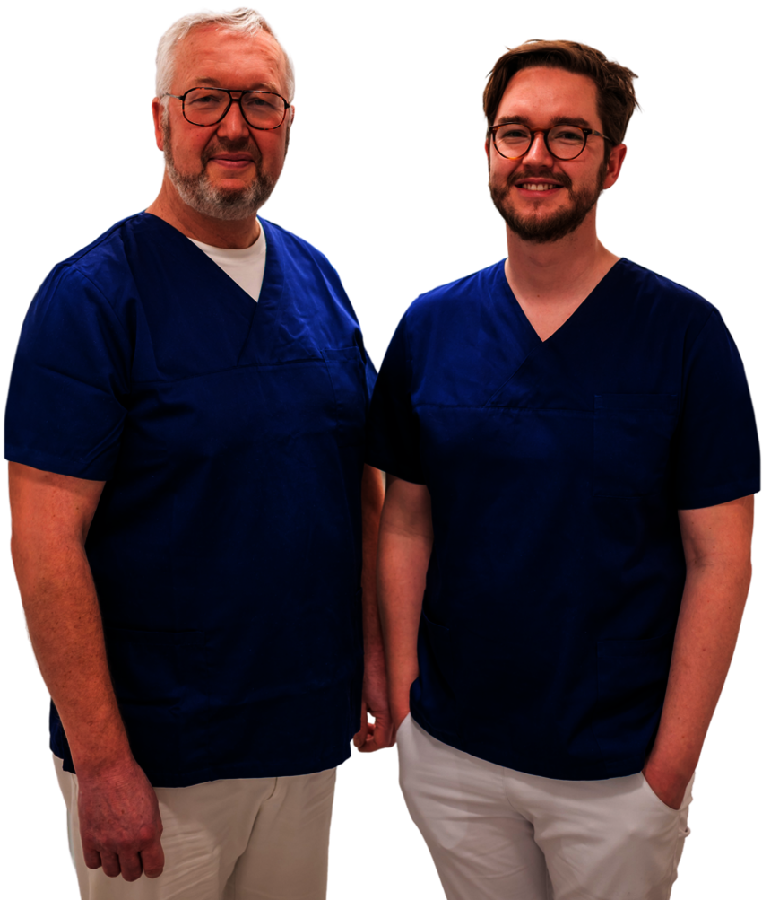 Die zwei Ärzte Dr. Karsten Hedderich und Dr. Ekkehart Hedderich stehen lächelnd in blauen OP-Kitteln und vor weißem Hintergrund beisammen.